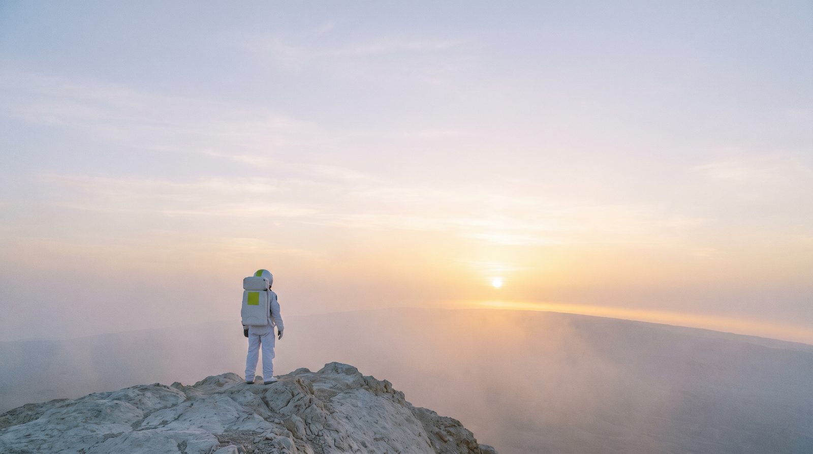 An astronaut standing on a ridge at sunrise, looking towards the horizon